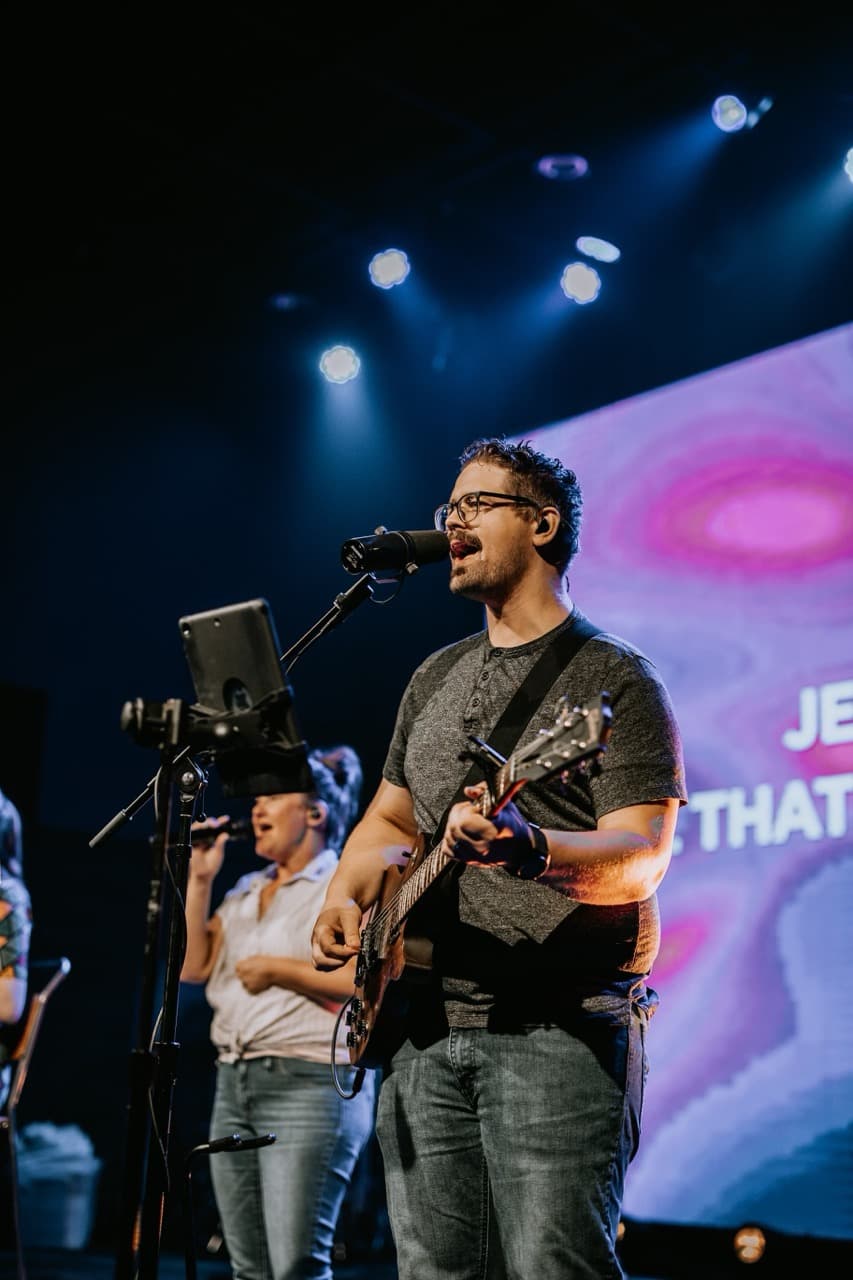 Worship leader playing guitar and singing on stage at Pleasant Valley.
